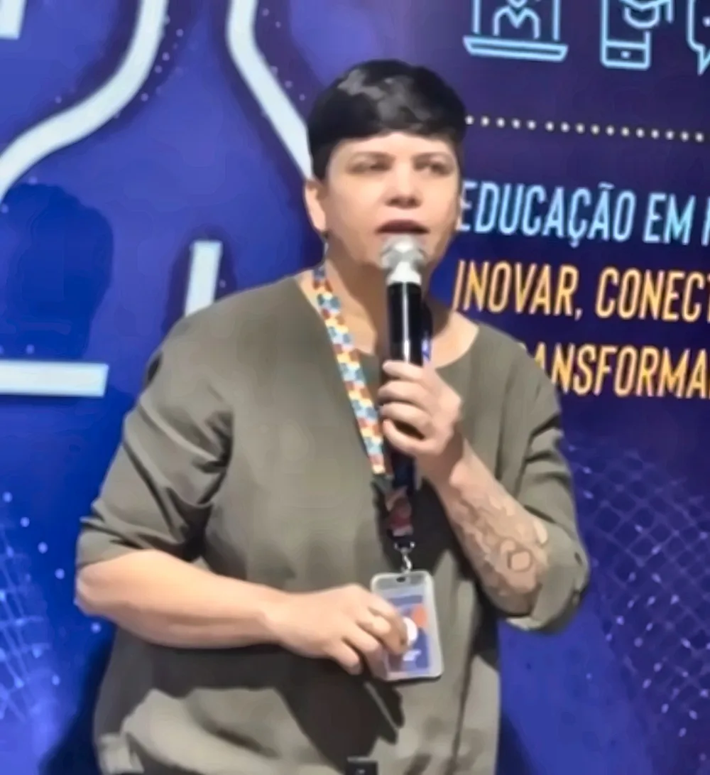 Maristela de microfone na mão, falando para professores em frente a um painel azul de evento